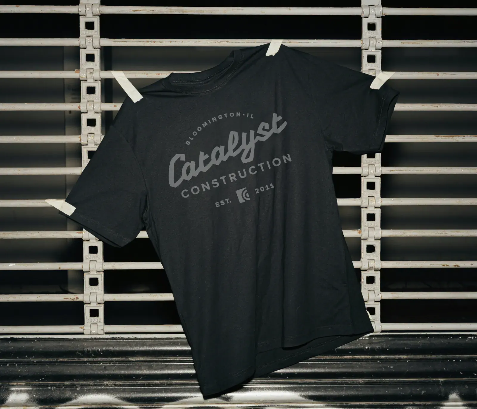 Black Catalyst Construction shirt displayed against an industrial metal rack