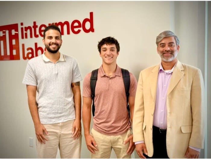 Three people standing together in front of an Intermed Labs sign